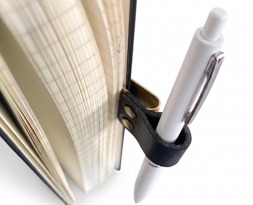 Black leather pen holder clips attached to notebook pages holding a daily writing pen.