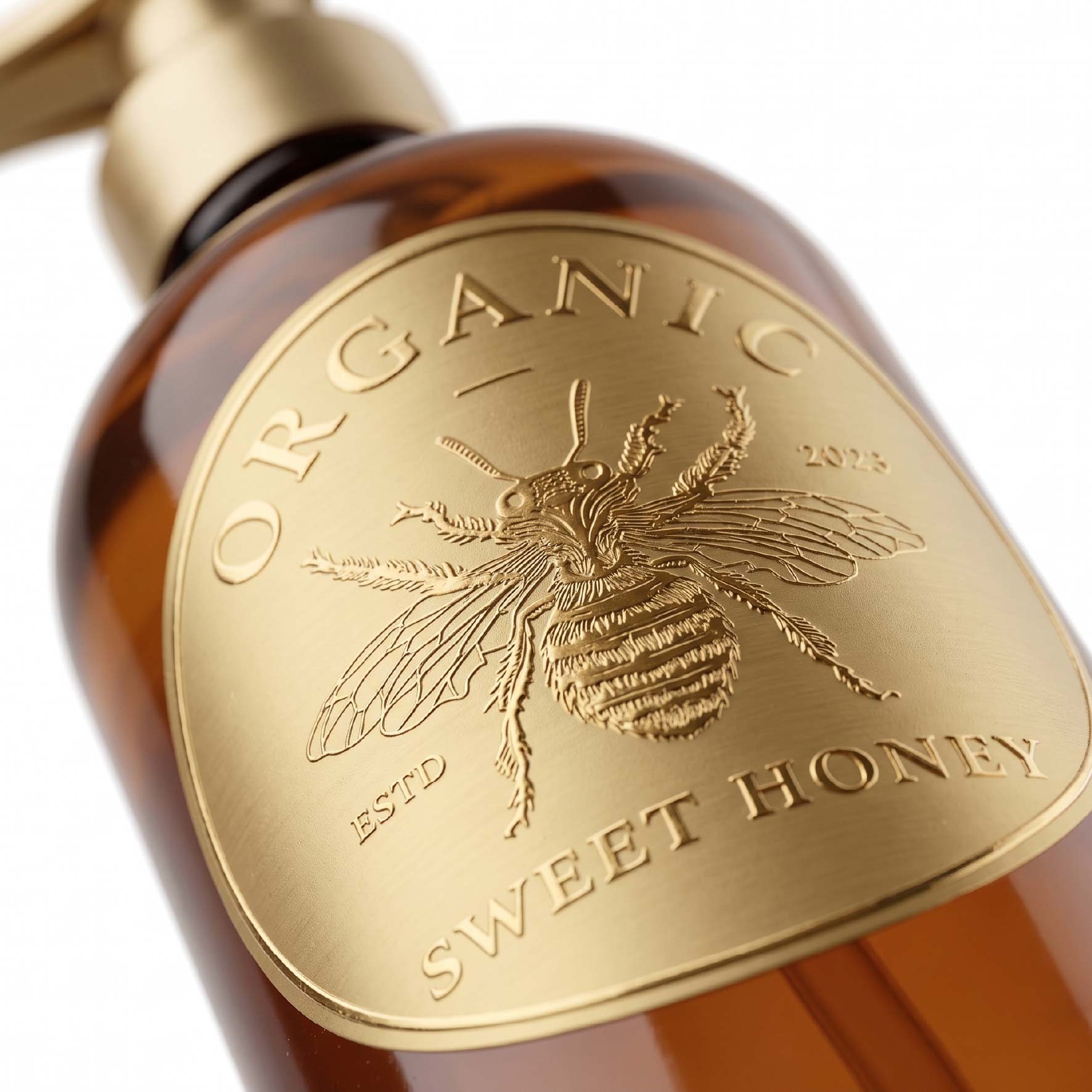 Large gold metal label with detailed bee artwork displayed on an amber bottle