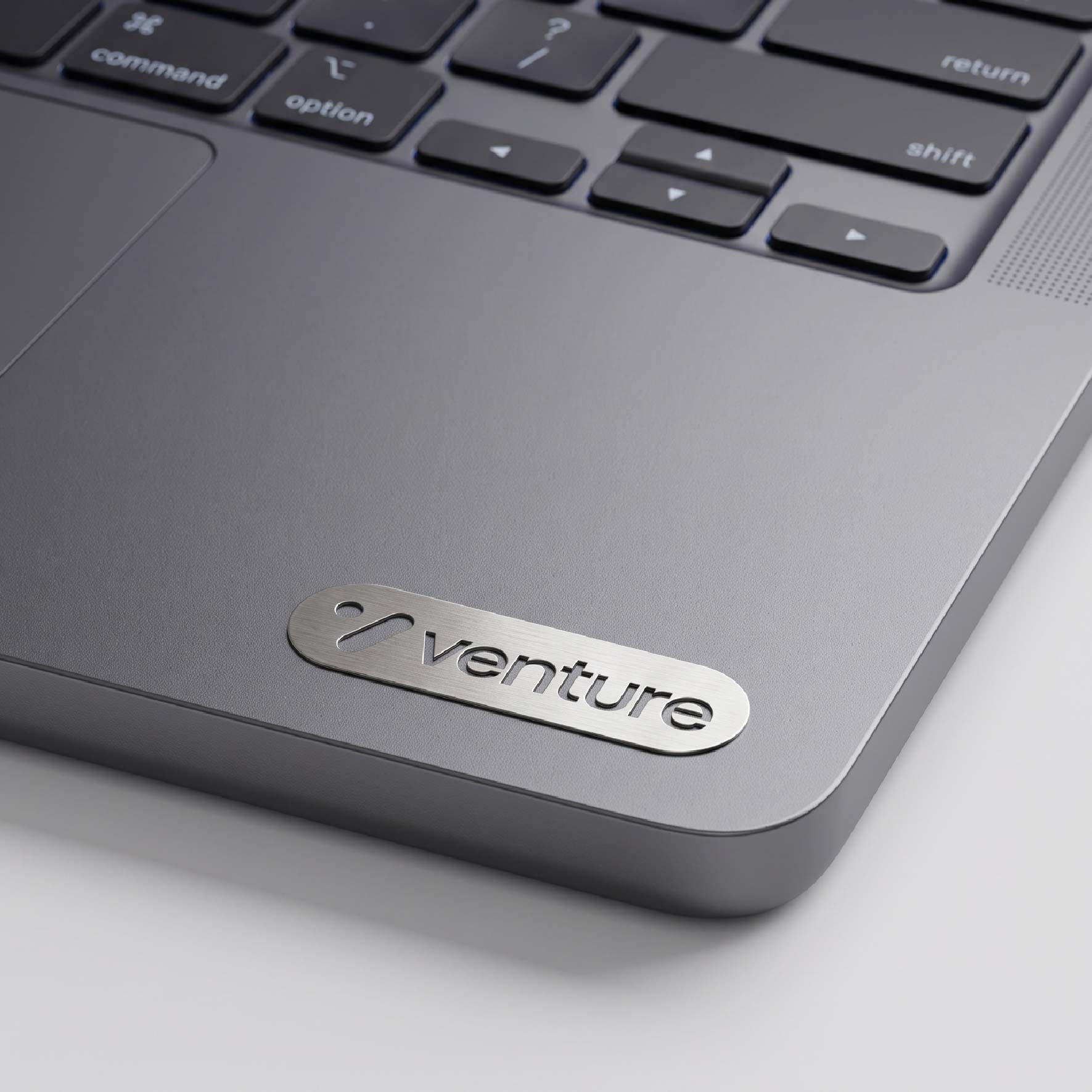 Slim brushed metal nameplate placed on a laptop surface with cut-out lettering